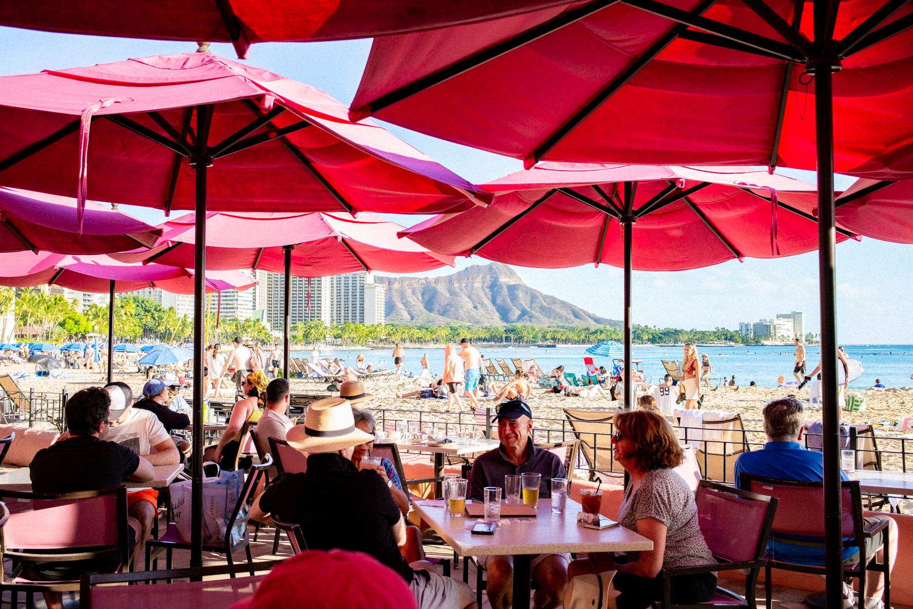 Diamond Head and Waikiki Beach seen from under the red umbrellas of a beachfront bar in Honolulu